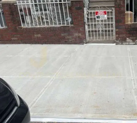 Finished sidewalk flags in front of a brick building with barred windows and a gate