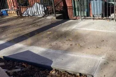 Finished concrete sidewalk flags with autumn leaves beside an iron railing