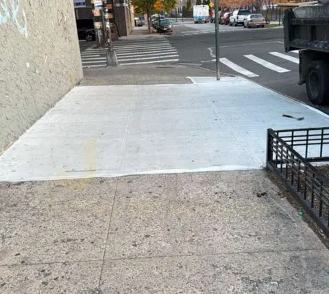 New concrete sidewalk slab at a street corner beside a crosswalk