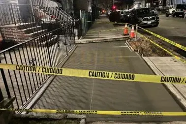 Newly poured sidewalk along an iron railing and front stoops, taped off while it cures