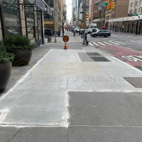 New concrete sidewalk slabs outside storefronts on a city avenue lined with high-rise buildings