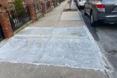 Newly replaced concrete sidewalk flags along a row of brick homes with iron front railings