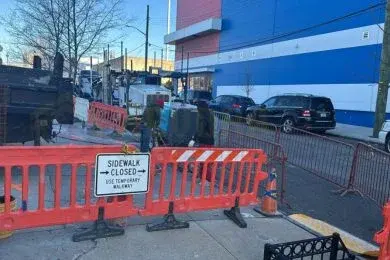 Orange barriers and a sidewalk-closed sign pointing to a temporary walkway outside a commercial building