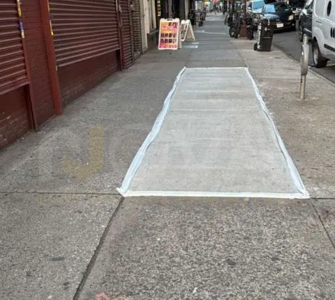 A single replaced sidewalk section, still outlined in white, set into an older sidewalk outside a storefront