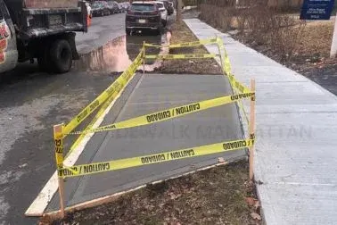 Wet concrete sidewalk section inside wooden forms, taped off beside a planted strip